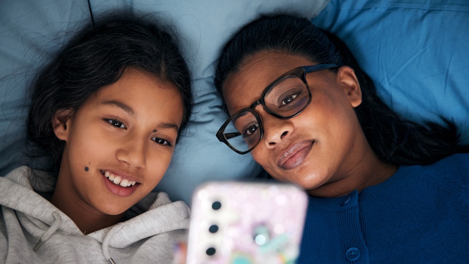 Mamma och dotter ligger i sängen och tittar på en mobilskärm