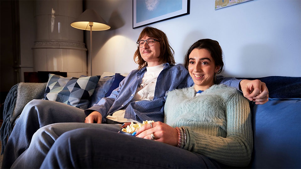 Glad kille och tjej sitter i soffan med en popcornskål och tittar på tv